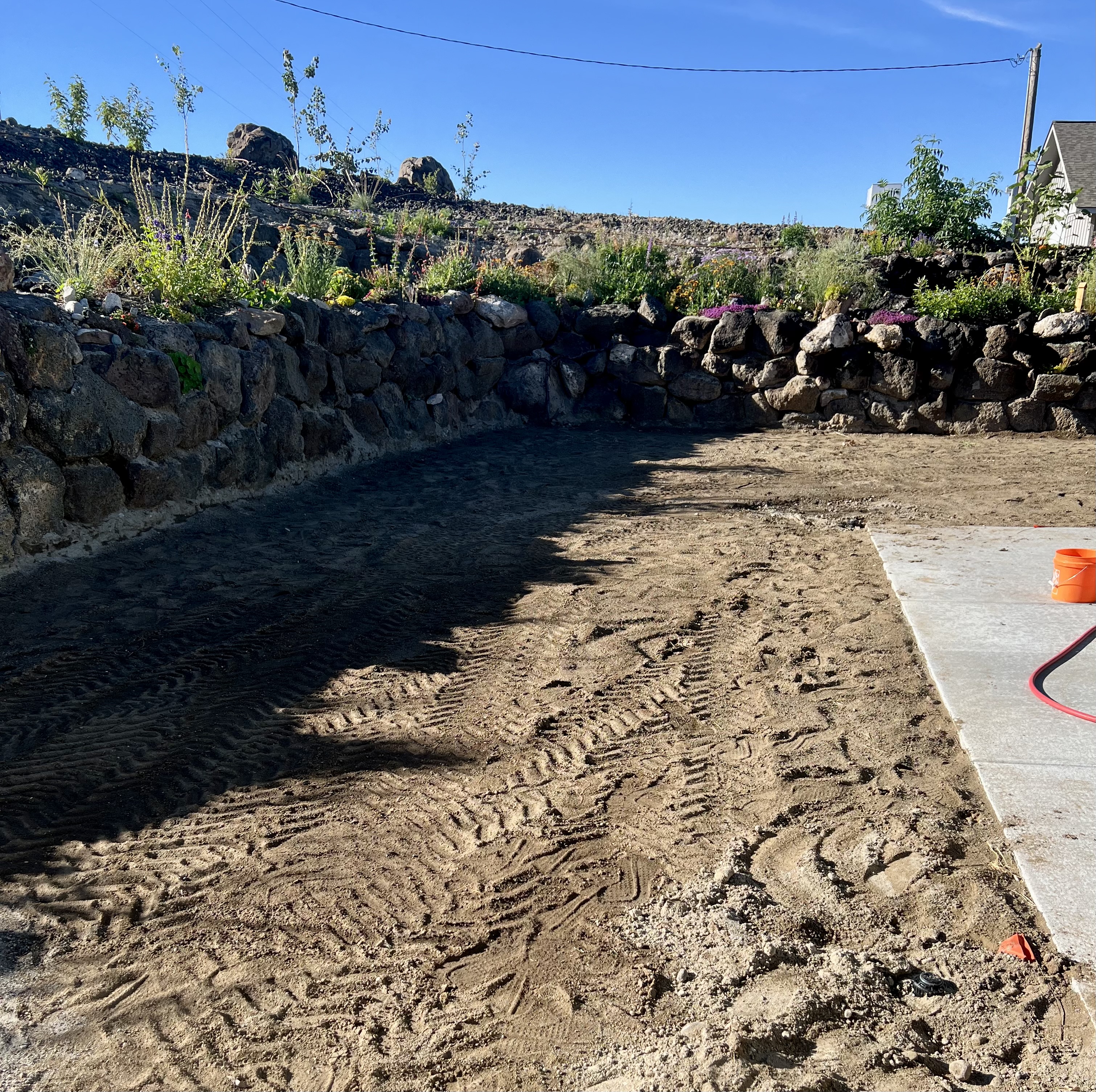 Bare graded dirt area before sod installation, bordered by a stone wall